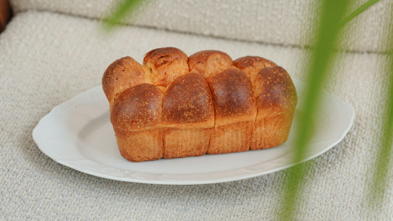 Golden brown brioche loaf on a white plate, placed on a neutral textured surface