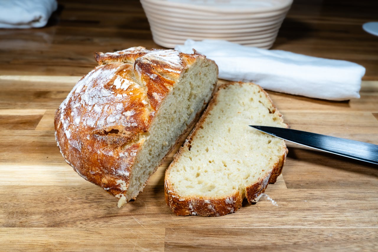 Crusty sourdough bread partially sliced on a wooden surface with a bread knife beside it