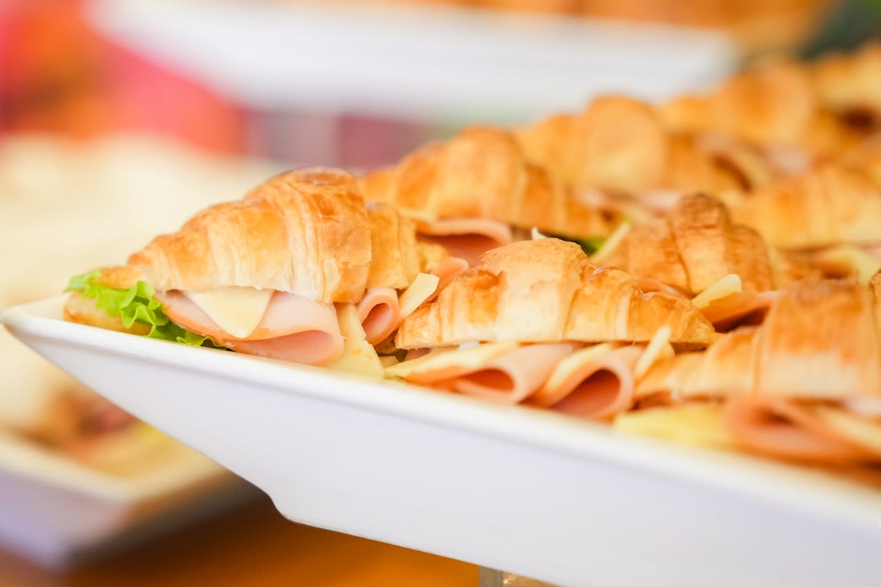 Ham and cheese croissant sandwiches arranged on a white serving tray
