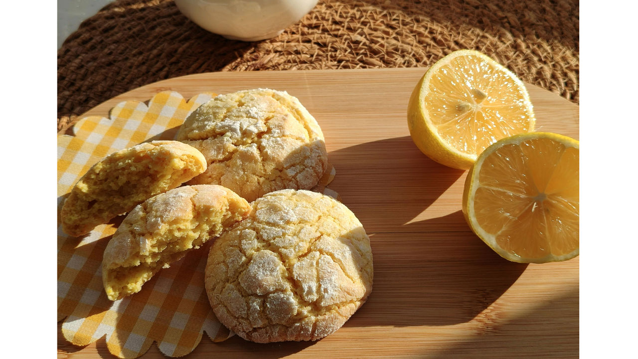 Lemon crinkle cookies with cracked sugar tops next to fresh lemon halves on a wooden board