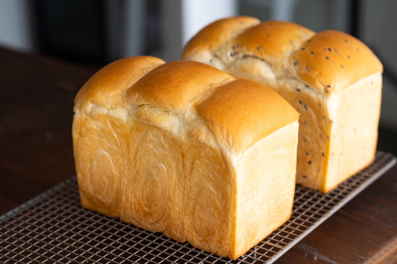 Two fluffy loaves of Japanese milk bread cooling on a wire rack, one plain and one with black sesame seeds