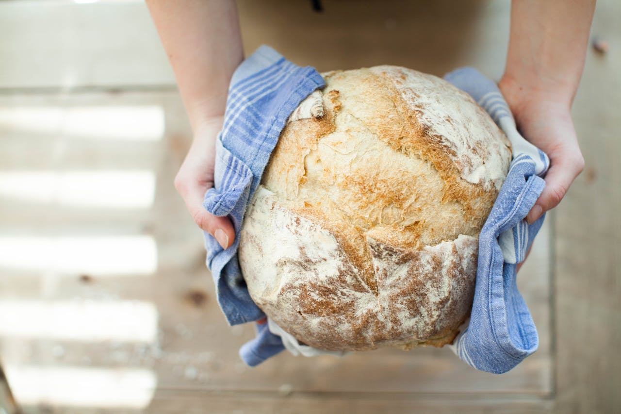 Round artisan bread loaf held in a blue-striped towel by both hands