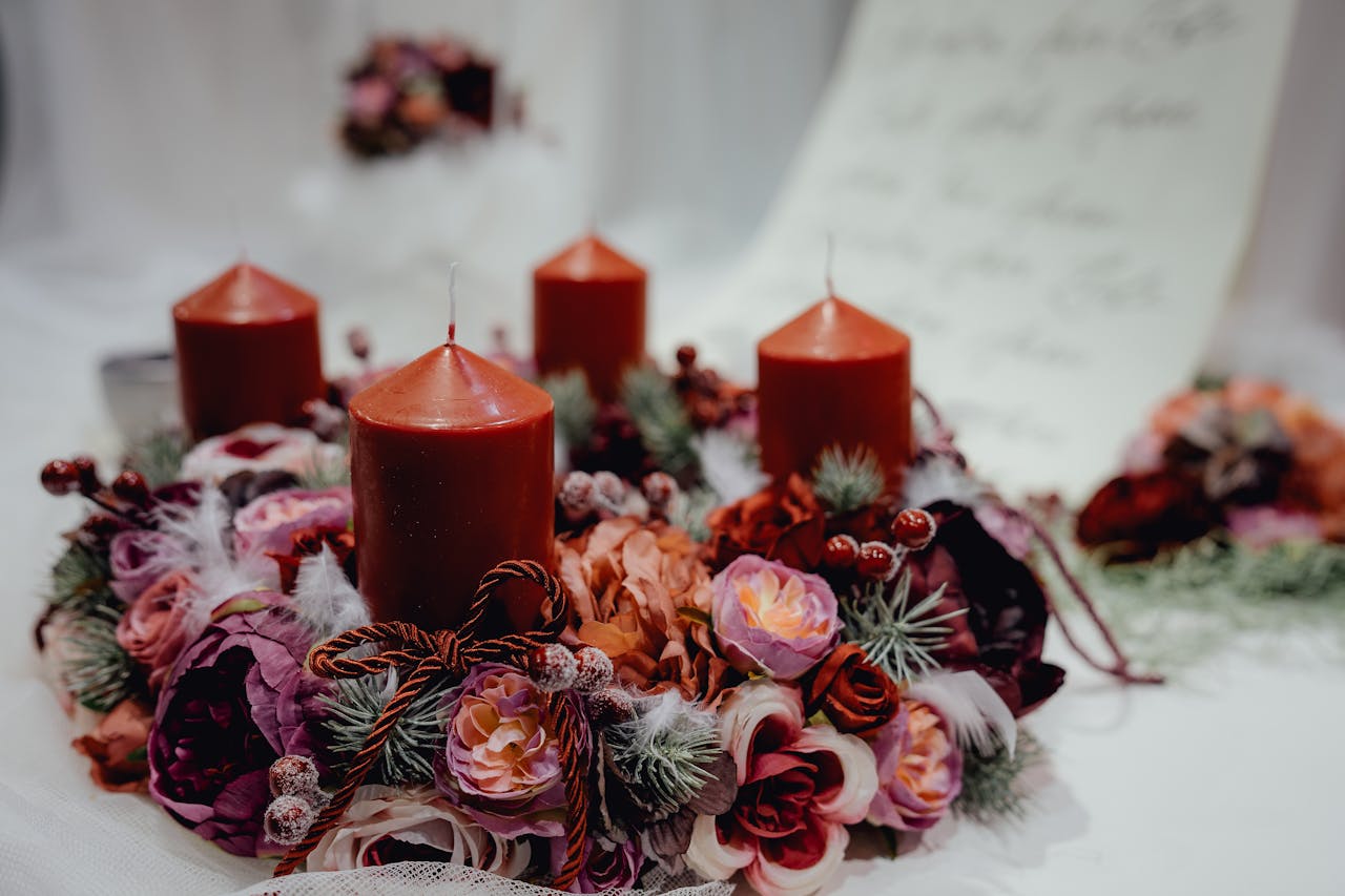 Red candle wreath centerpiece with dried flowers, berries, pine accents, and decorative ribbon on white fabric