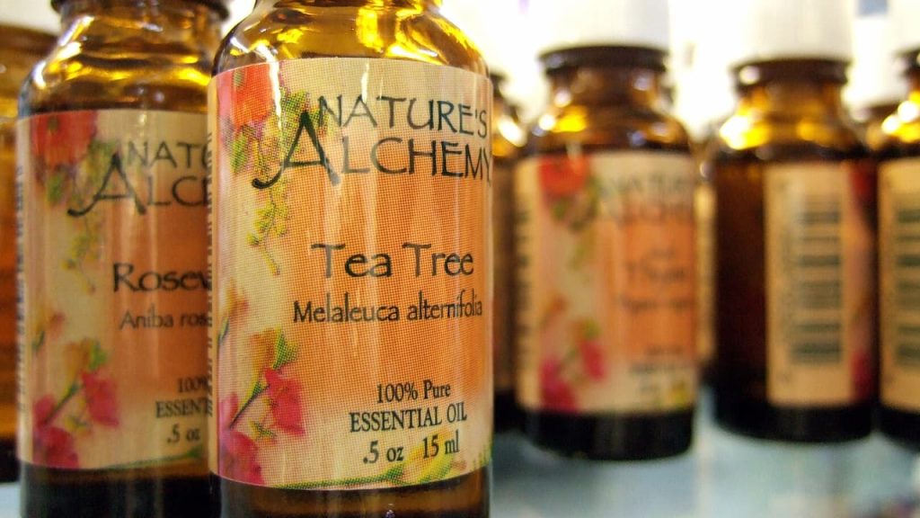 Row of Nature's Alchemy essential oil bottles in amber glass, featuring Tea Tree and Rose varieties with floral labels