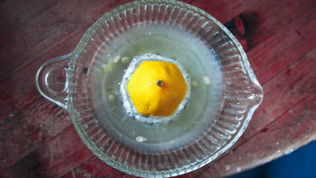 Glass citrus juicer with half an lemon placed on wooden surface, showing ridged reaming cone and collection bowl
