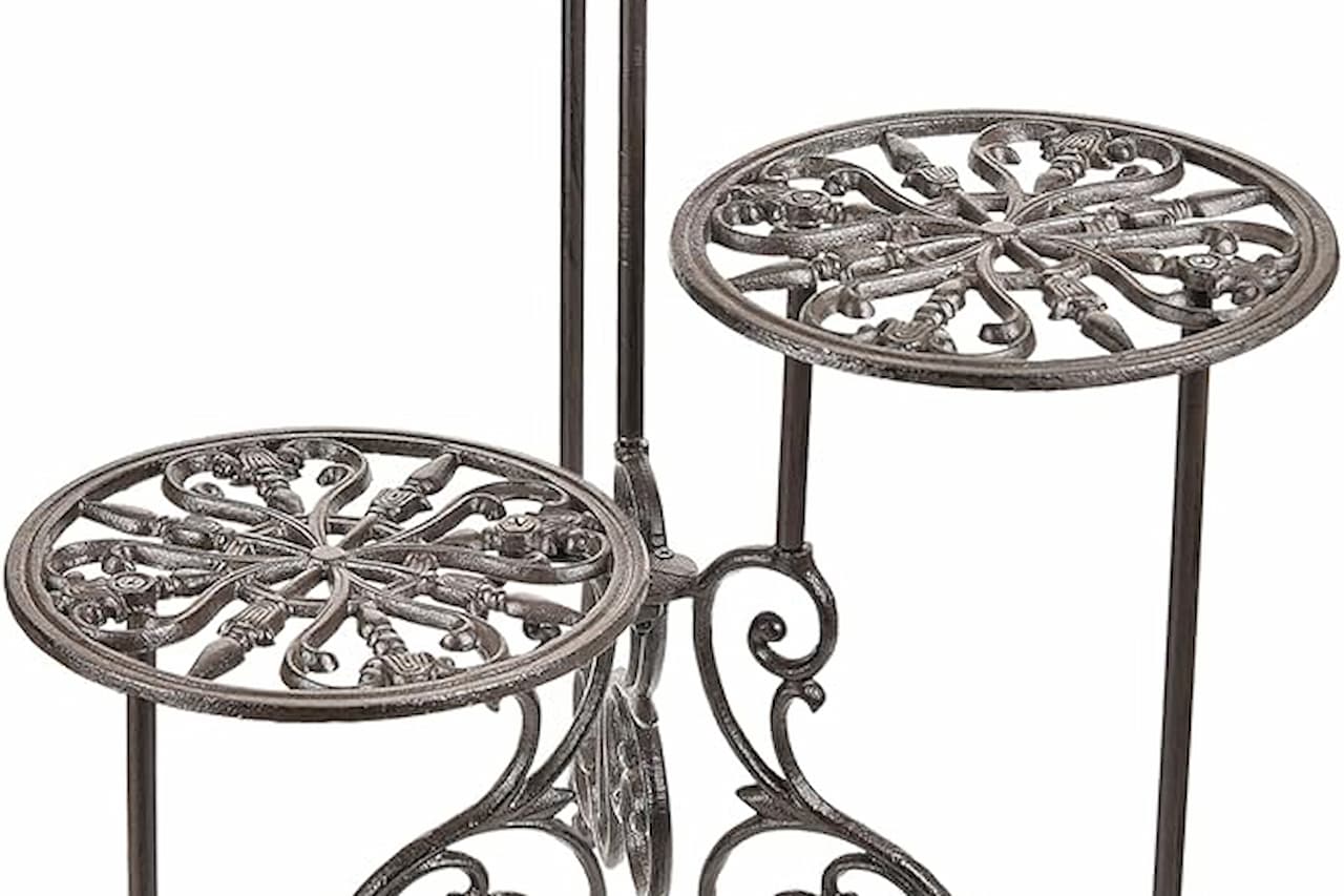 Decorative wrought iron plant stand with two circular, intricately patterned platforms and elegant scrollwork on the legs, in a dark bronze finish
