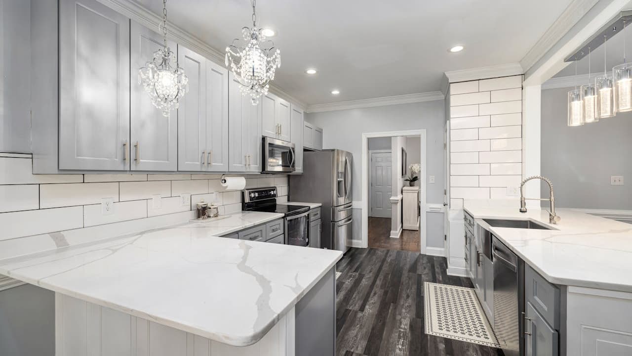 Modern gray and white kitchen with marble countertops, subway tile backsplash, crystal chandeliers, stainless steel appliances, dark hardwood floors