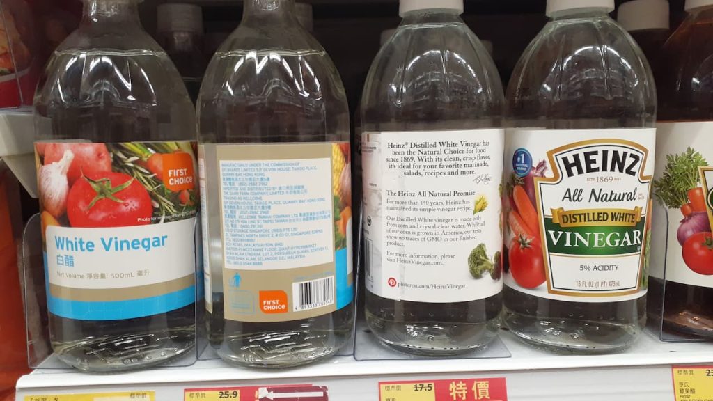 tore shelf displaying white vinegar bottles including First Choice and Heinz brands with price tags below.