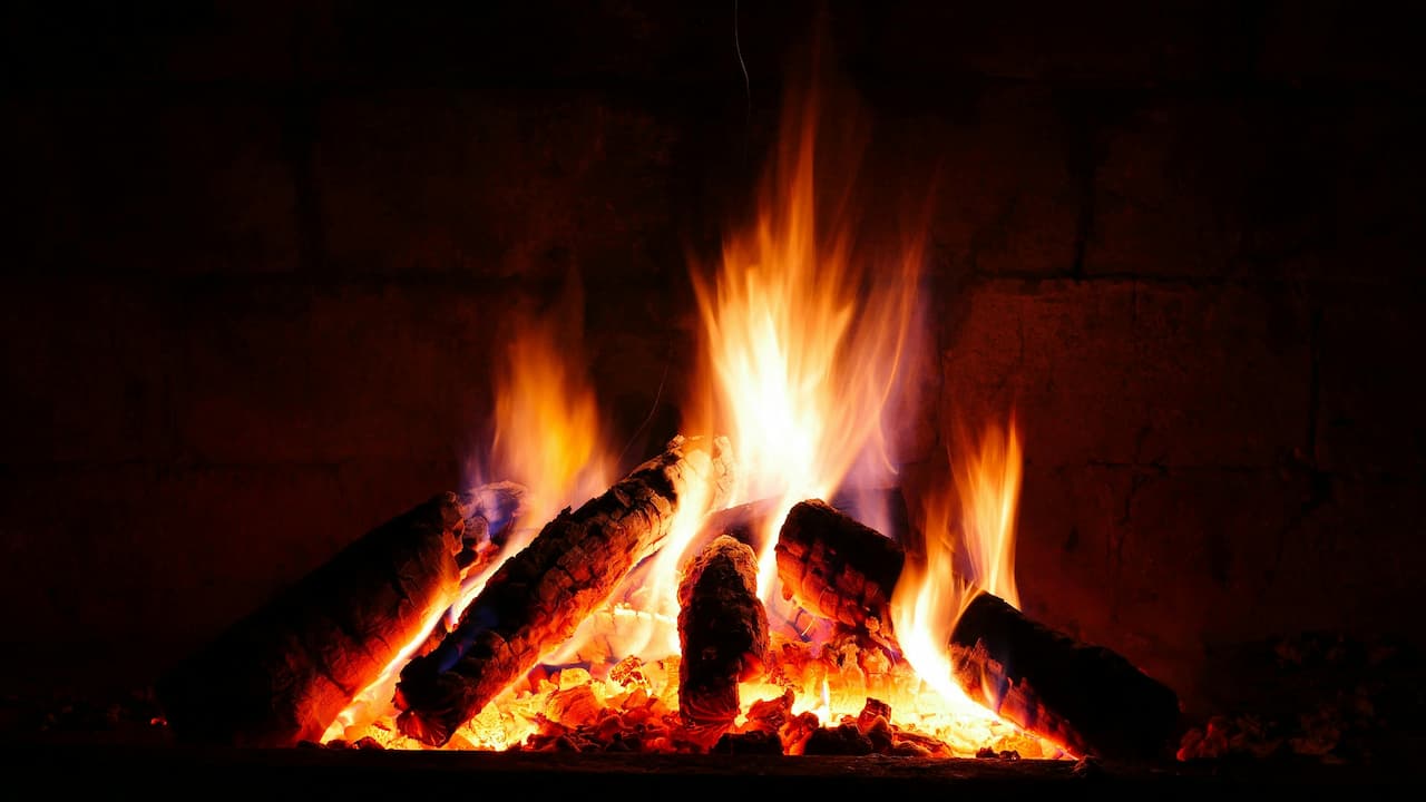 Burning logs in a fireplace, bright orange and yellow flames, glowing embers beneath