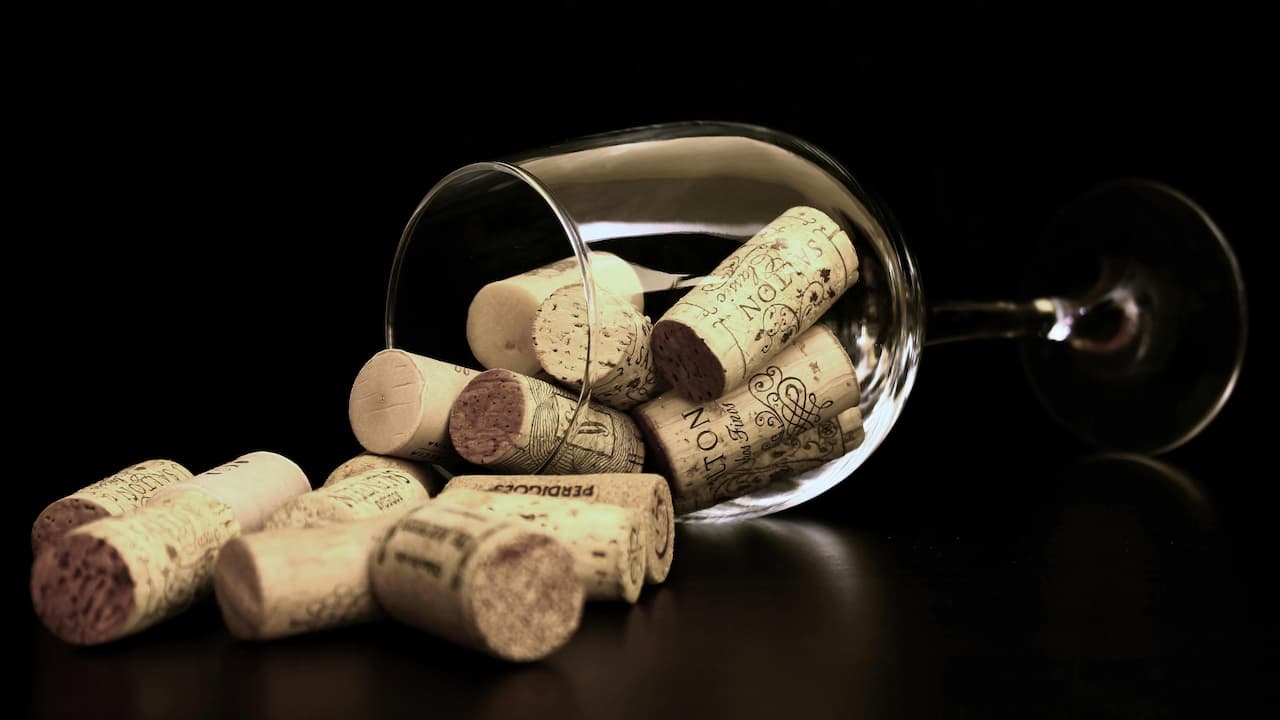 Clear wine glass tipped over on a black surface, spilling out several wine corks with printed winery logos and names