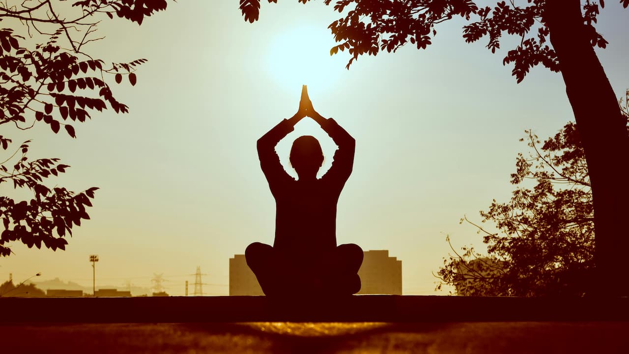 Silhouette of a person meditating in a seated yoga pose with hands raised in prayer position