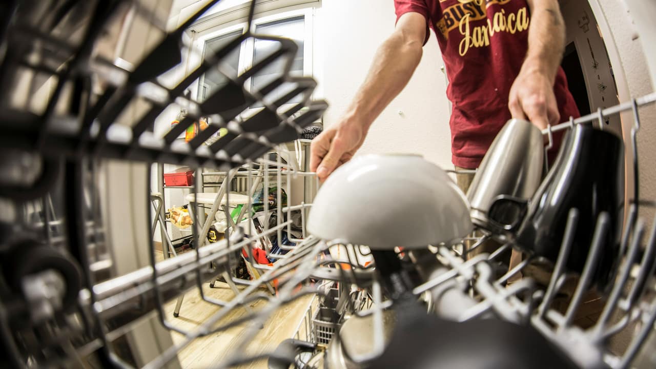 Person unloading dishes from a dishwasher, view from inside the dishwasher rack, with clean mugs and a bowl in the foreground
