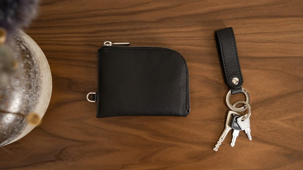 Black leather wallet and keychain with keys placed on wooden table next to decorative ceramic bowl