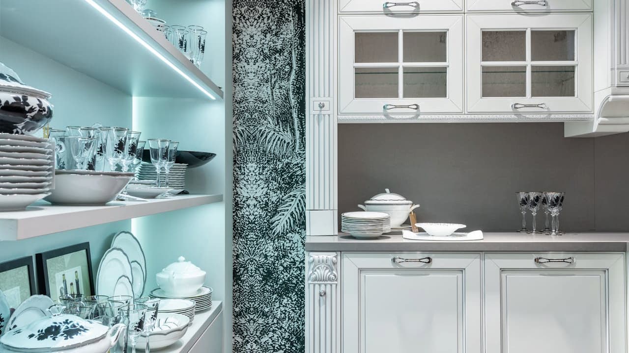 Elegant kitchen with white cabinets, open shelving displaying dishes and glassware, LED lighting, and ornate wallpaper accent