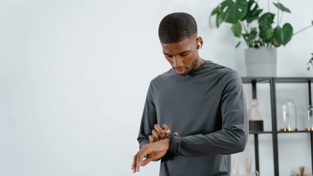 Black man in gray long-sleeve shirt setting timer on his watch in modern room with plants and shelving