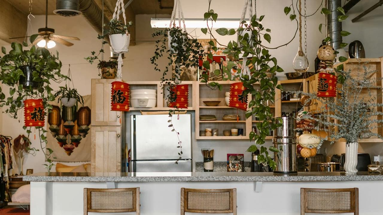 Bohemian kitchen with hanging plants, red Chinese lanterns, open shelving, granite countertop, and cane-back bar stools creating eclectic style