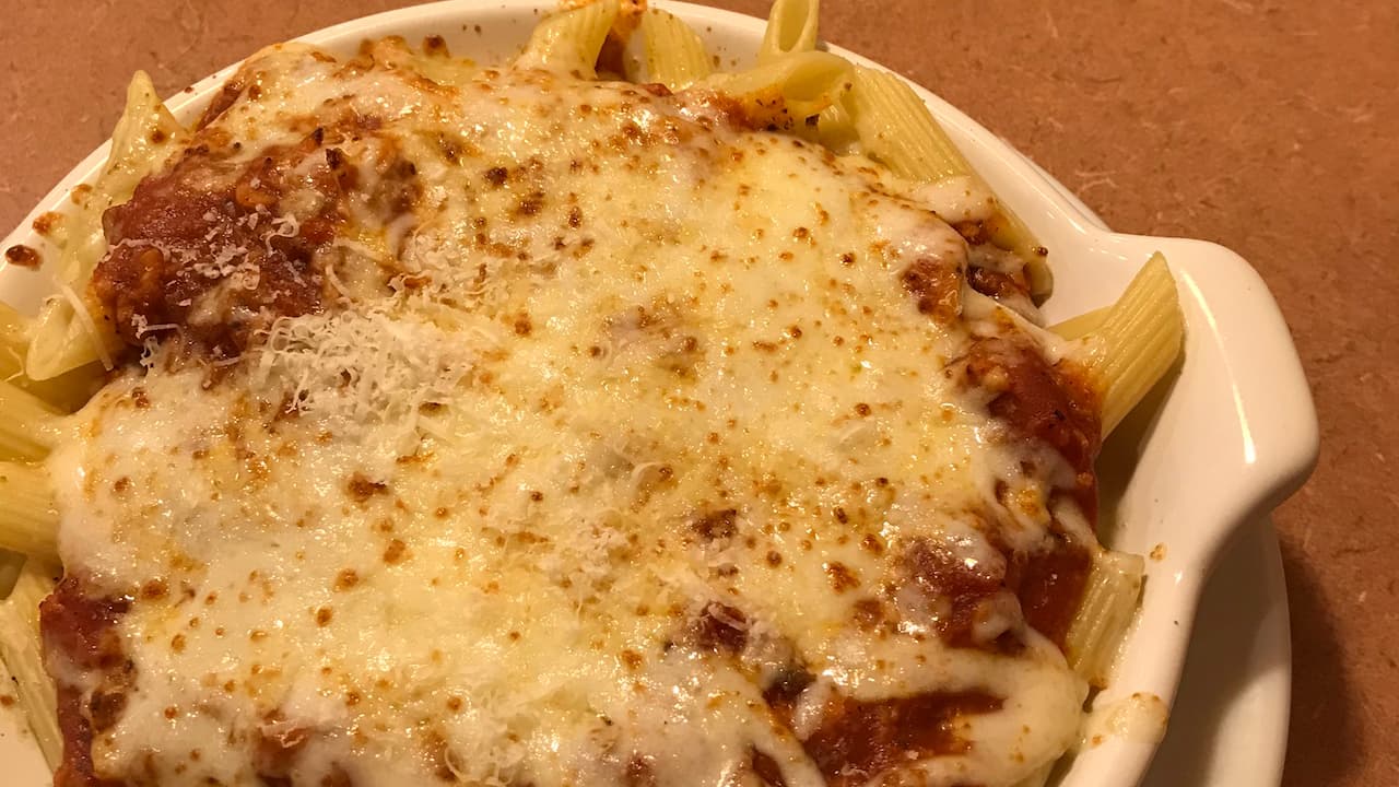 Baked ziti in a white ceramic dish, topped with marinara sauce and a generous layer of melted, golden-brown cheese
