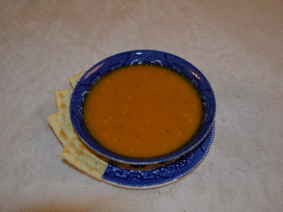 Blue patterned bowl filled with orange butternut squash soup, served with rectangular saltine crackers on a matching plate, placed on a white textured tablecloth