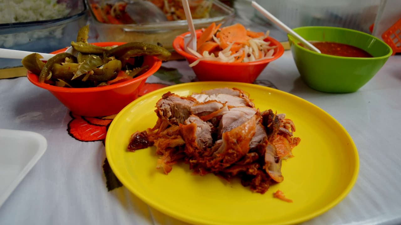 Shredded carnitas pork served on a yellow plate, accompanied by small bowls of pickled jalapeños, sliced carrots with onions