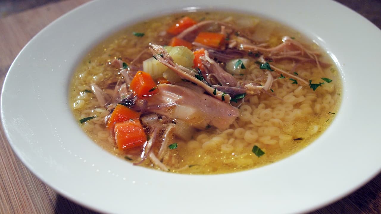 Bowl of chicken noodle soup with shredded chicken, diced carrots, celery, parsley, and small round pasta in a clear broth, served in a white dish