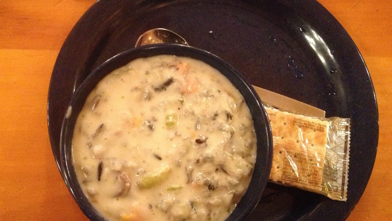 Bowl of creamy chicken and wild rice soup served on a dark plate with a packet of saltine crackers and a spoon