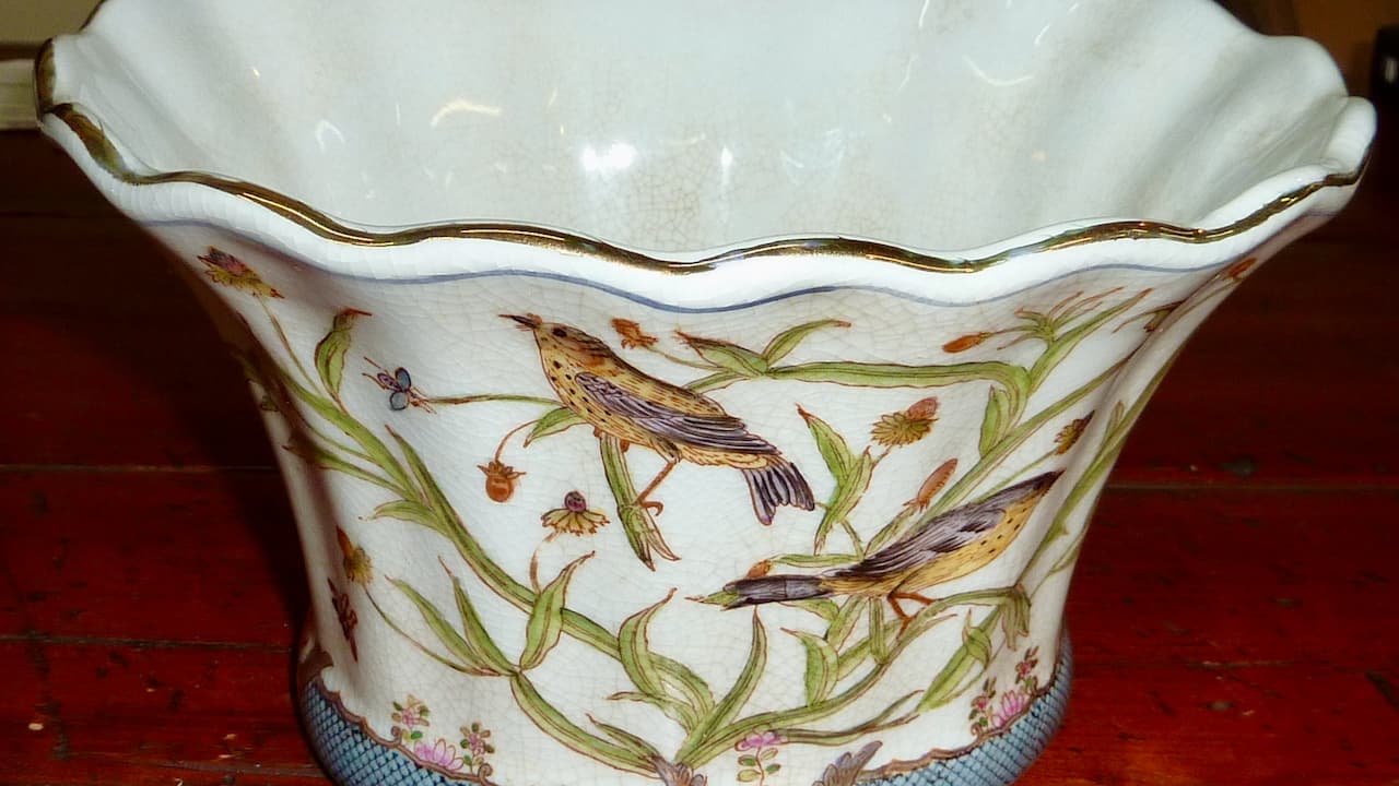 White porcelain vase with scalloped rim and gold trim, featuring hand-painted birds perched among green foliage and wildflowers