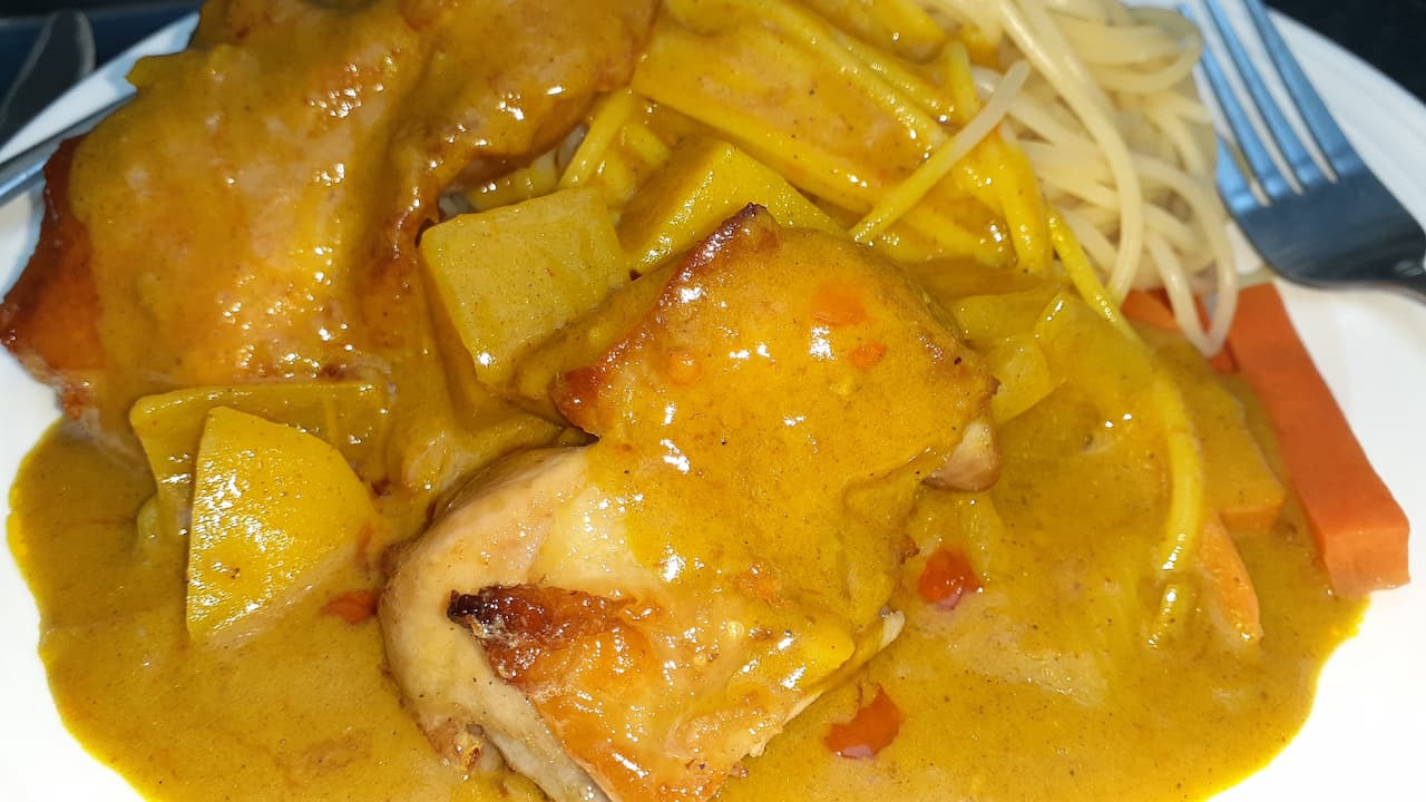 Plate of yellow curry chicken with potato chunks and spaghetti noodles, served alongside carrot sticks and topped with a rich, glossy curry sauce