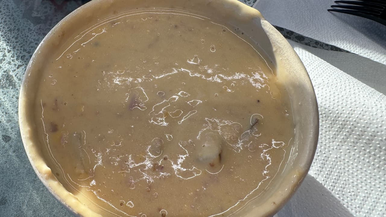 Bowl of creamy potato soup with visible chunks of potato and bacon, served on a table beside a paper napkin and black plastic cutlery