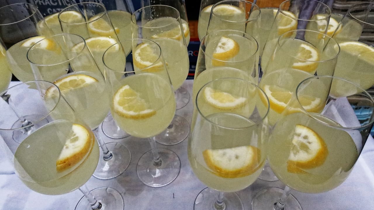 Multiple glasses of pale yellow limoncello spritz garnished with lemon slices, arranged closely on a table for serving