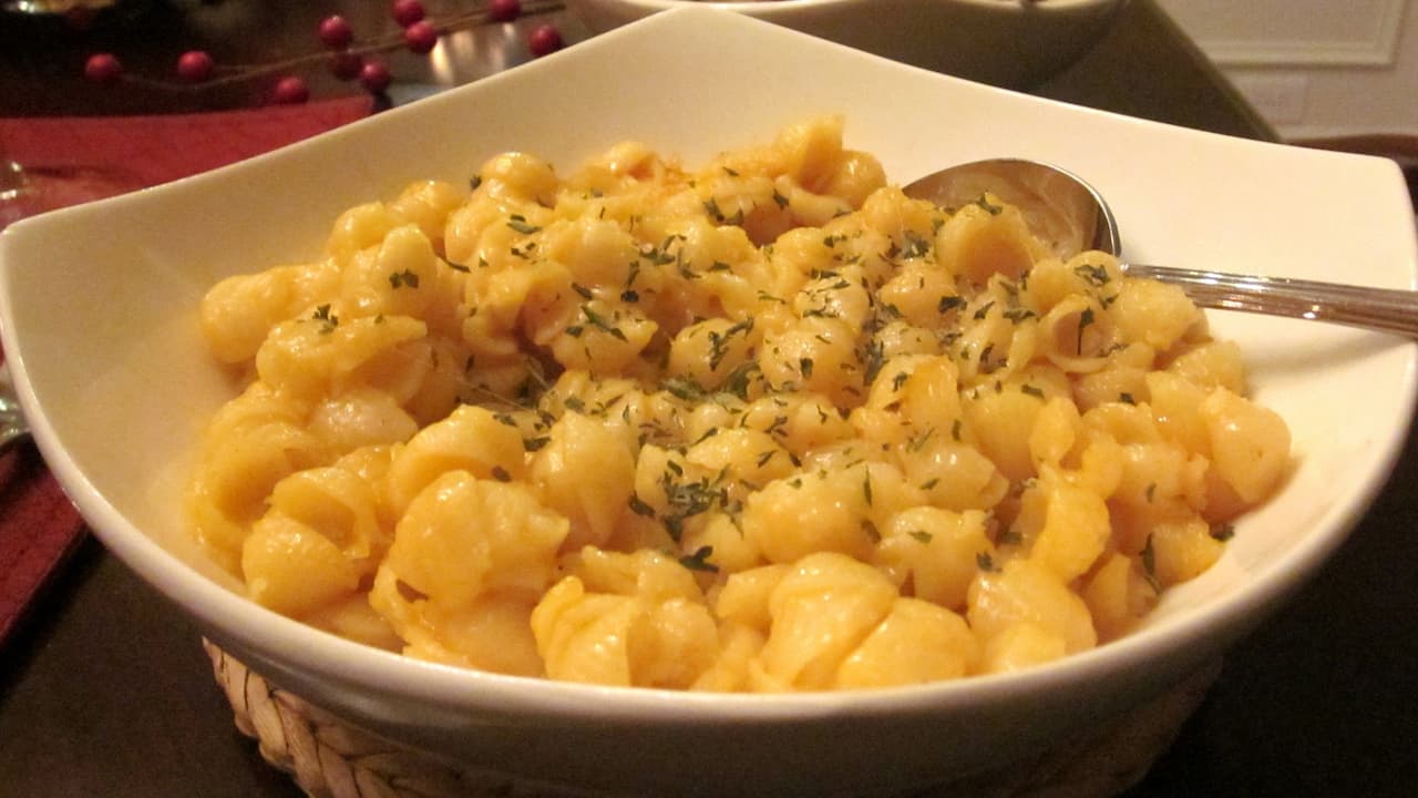 Shell pasta macaroni and cheese, creamy and golden, topped with a light sprinkle of herbs, served in a white bowl with a metal spoon