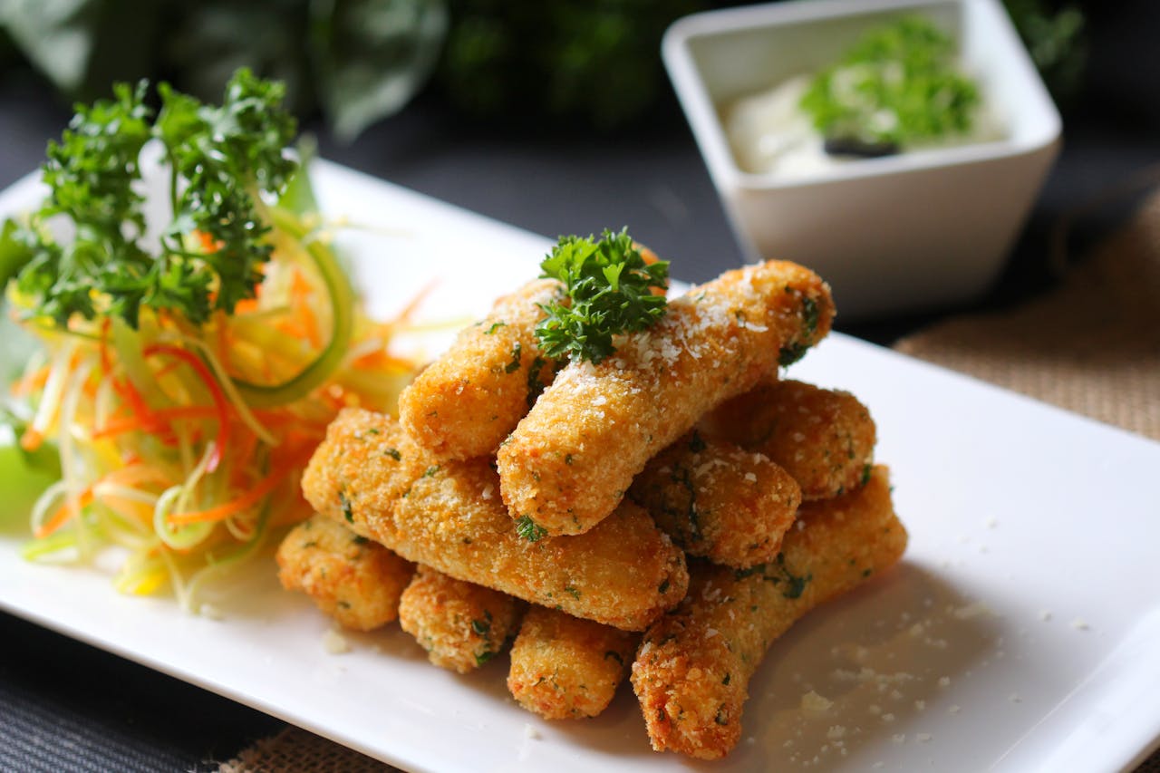 Golden mozzarella sticks stacked on a plate, garnished with parsley and served with shredded salad and dip
