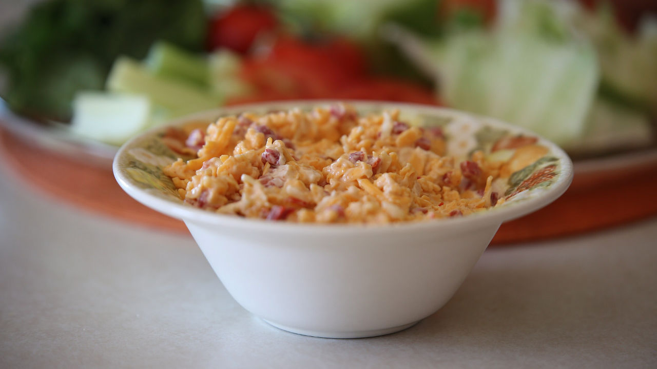 Bowl of creamy pimento cheese with shredded cheddar and diced red peppers on a table