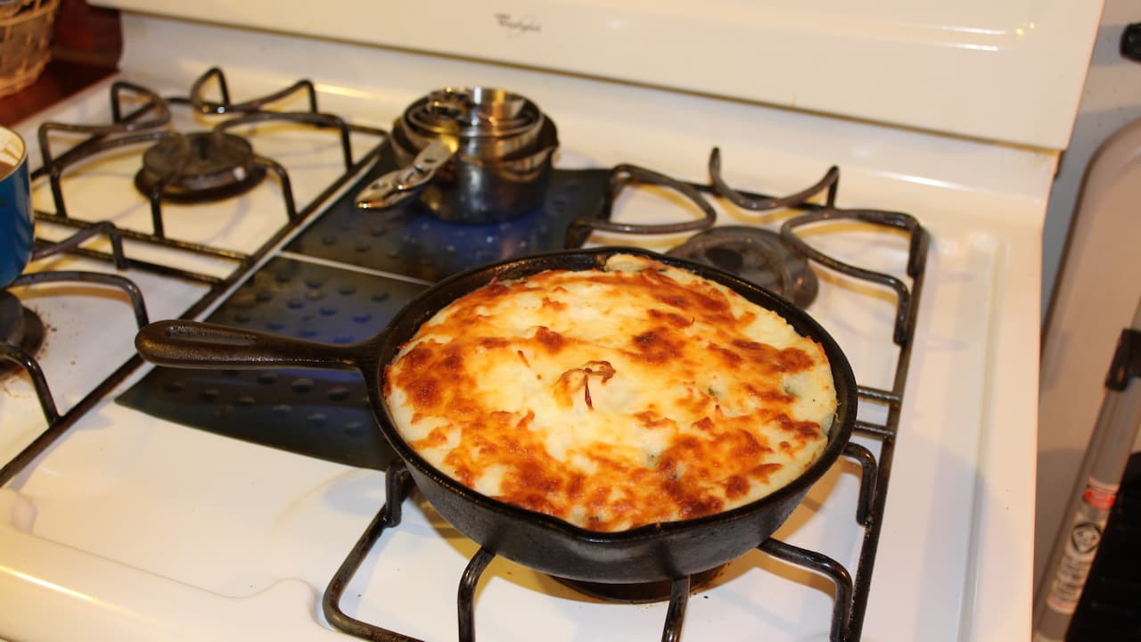 Shepherd’s pie topped with melted and browned mozzarella cheese, served in a black cast iron skillet on a gas stove