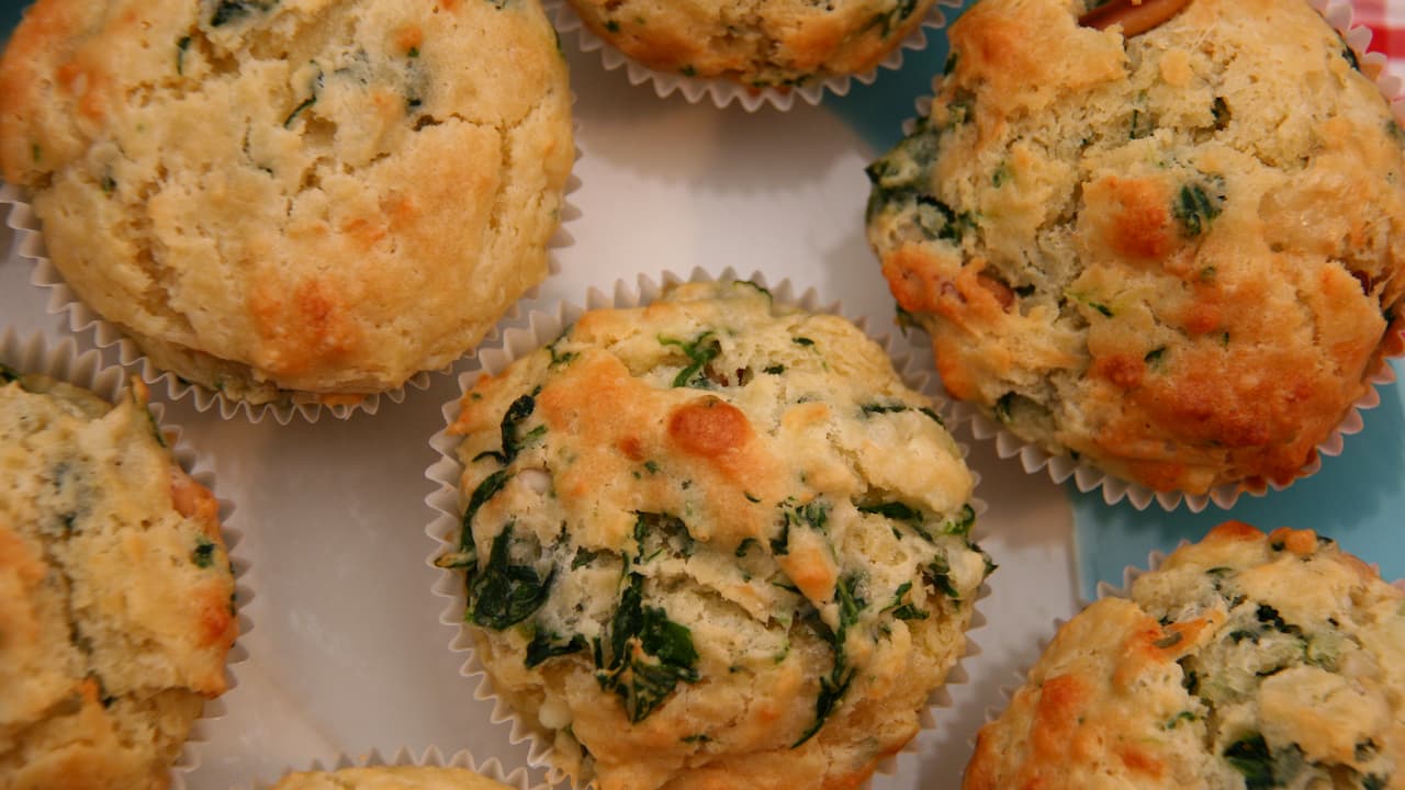Golden-brown savory stuffing muffins with visible green herbs and leafy vegetables, baked in white paper liners