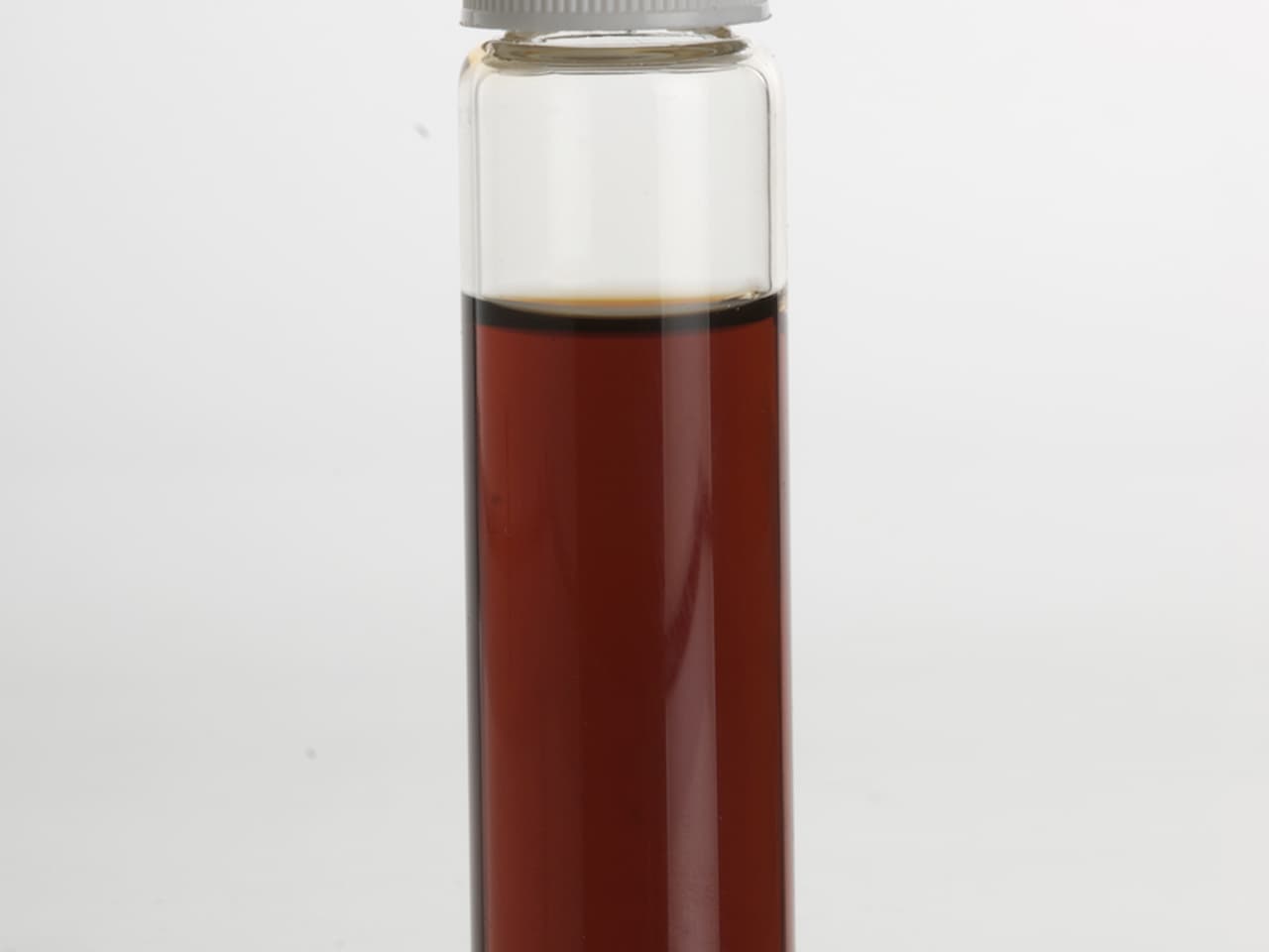 Clear glass bottle filled with dark brown liquid, sealed with a white cap, against a plain white background