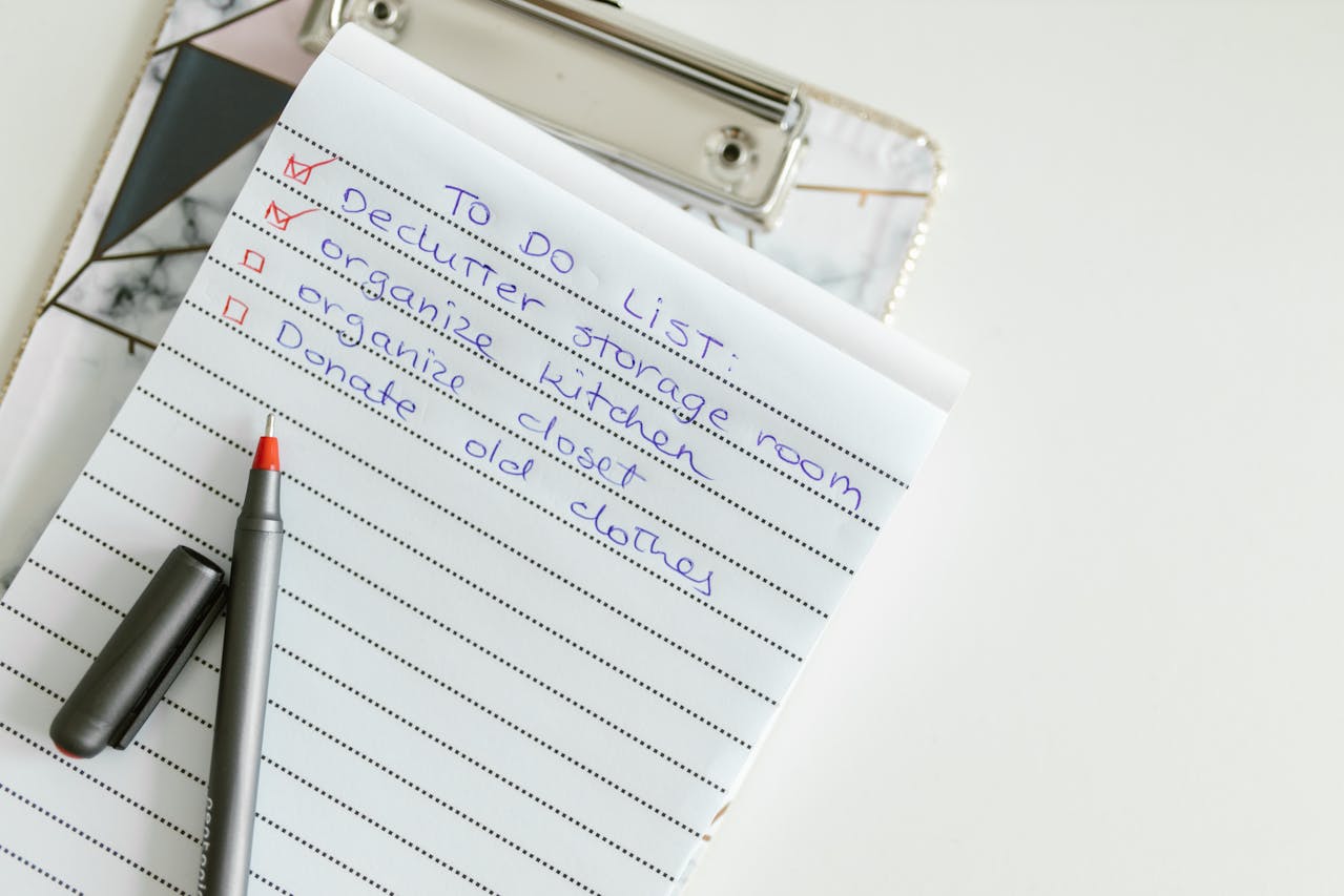 declutter to-do list on clipboard with red pen, handwritten tasks include storage, kitchen, closet, clothes donation