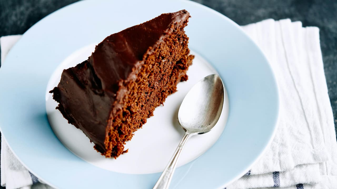 Slice of rich chocolate rum cake with dark chocolate frosting, served on a white and blue plate with a silver spoon