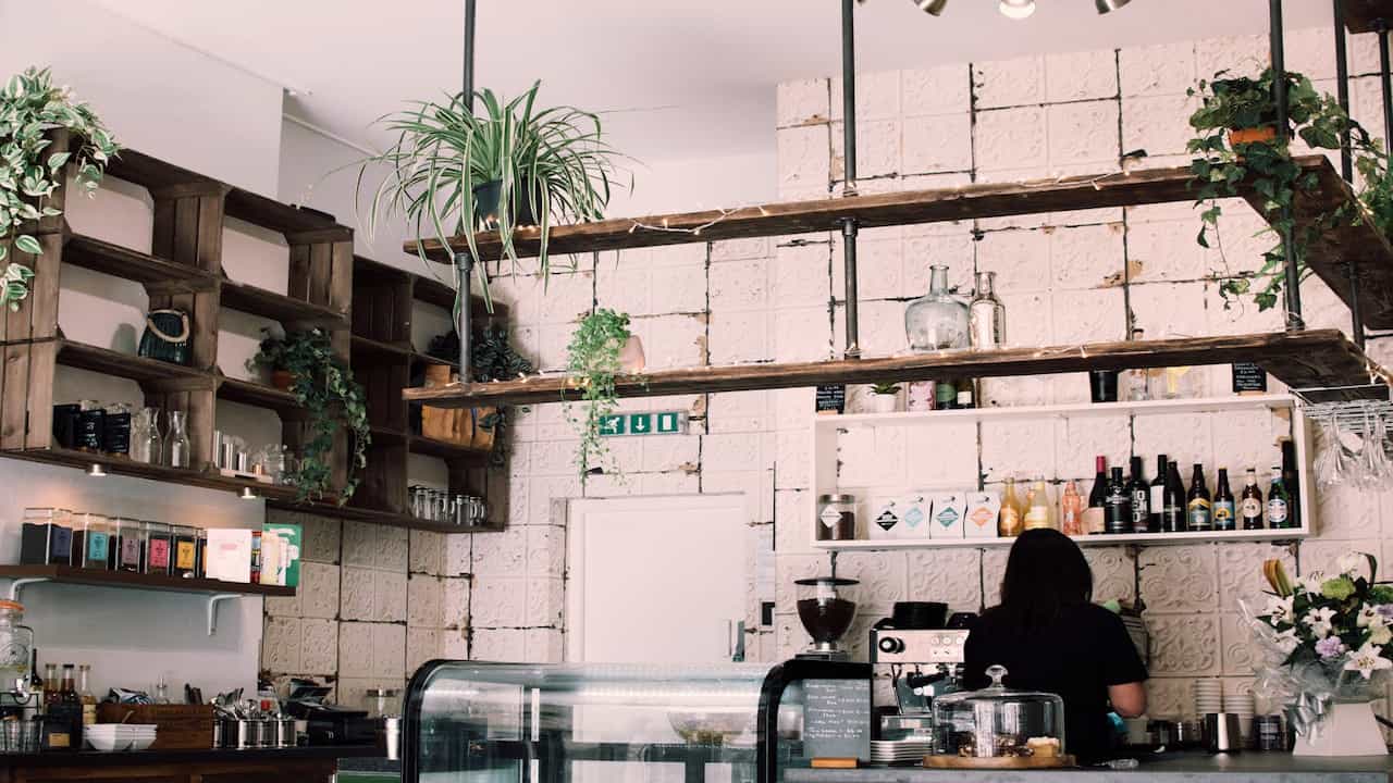 rustic kitchen with traditional white masonry stove, dried herbs hanging above, vintage kettle and cookware on stove, wooden walls and furniture, cozy warm lighting