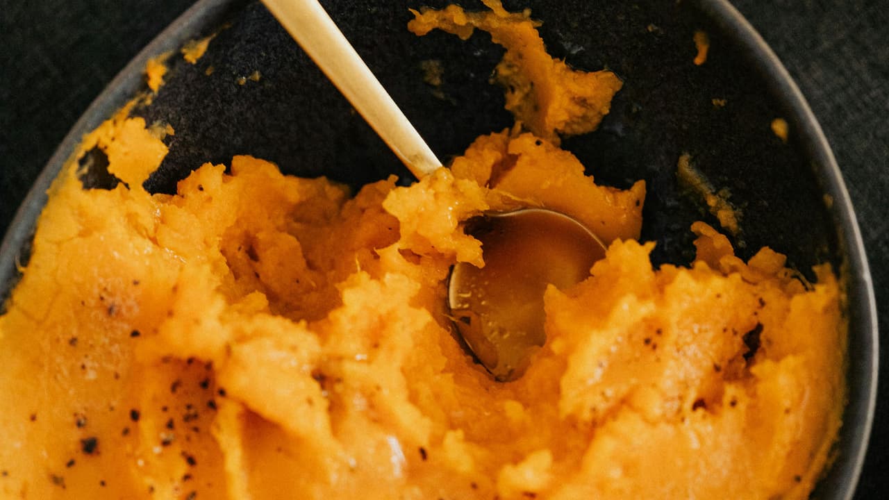 Creamy mashed sweet potatoes with black pepper, served in a dark bowl with a metal spoon