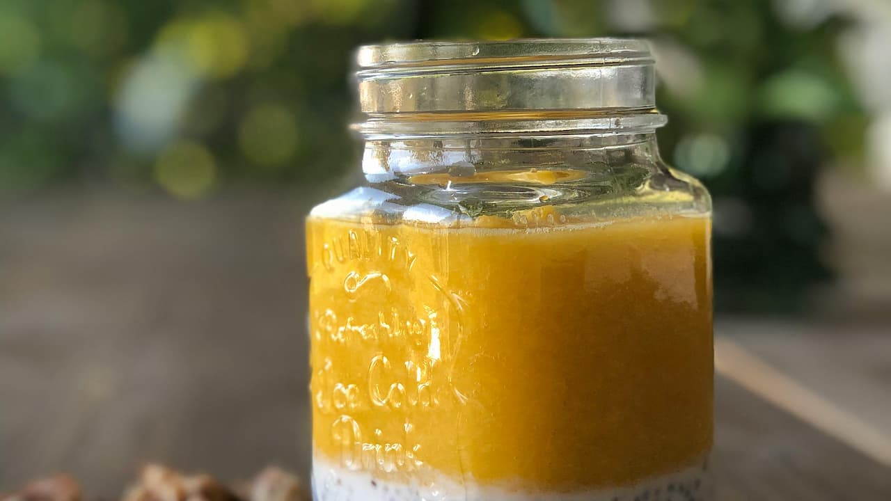 Jar of layered soup, with a white chia-like base topped by a thick, smooth orange layer, sealed with a metal lid, placed on a wooden surface