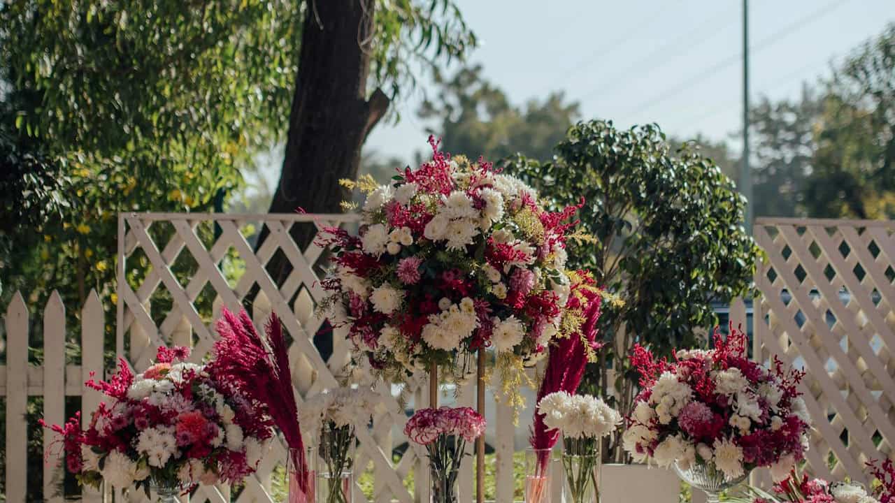 Outdoor floral arrangement display with large bouquets of white and dark pink flowers, including chrysanthemums and pampas grass