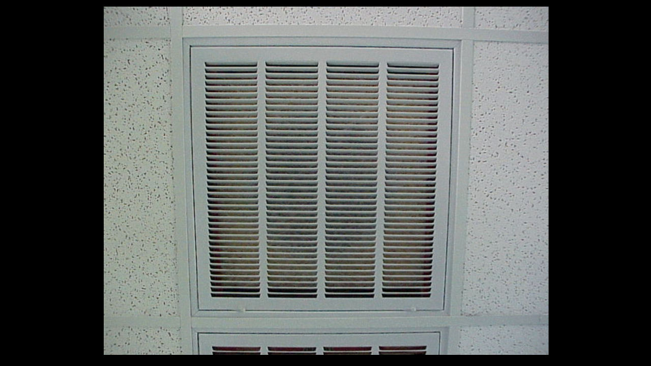 dusty rectangular ceiling air vent in white tile ceiling, likely part of HVAC or ventilation system