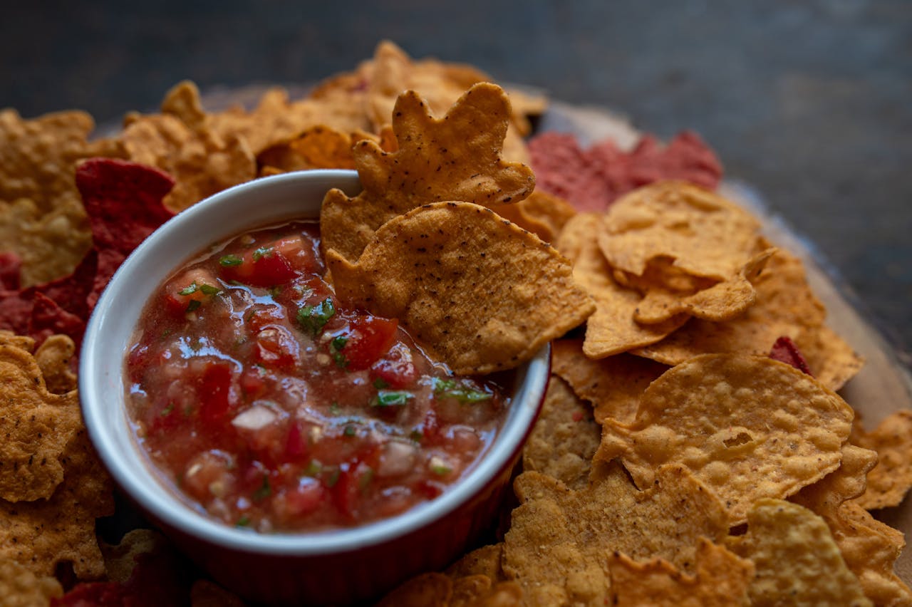 Tortilla chips surrounding a bowl of fresh tomato salsa on a wooden platter