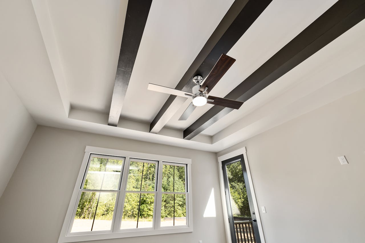 modern ceiling with dark wood beams and ceiling fan, large windows and glass door in bright empty room