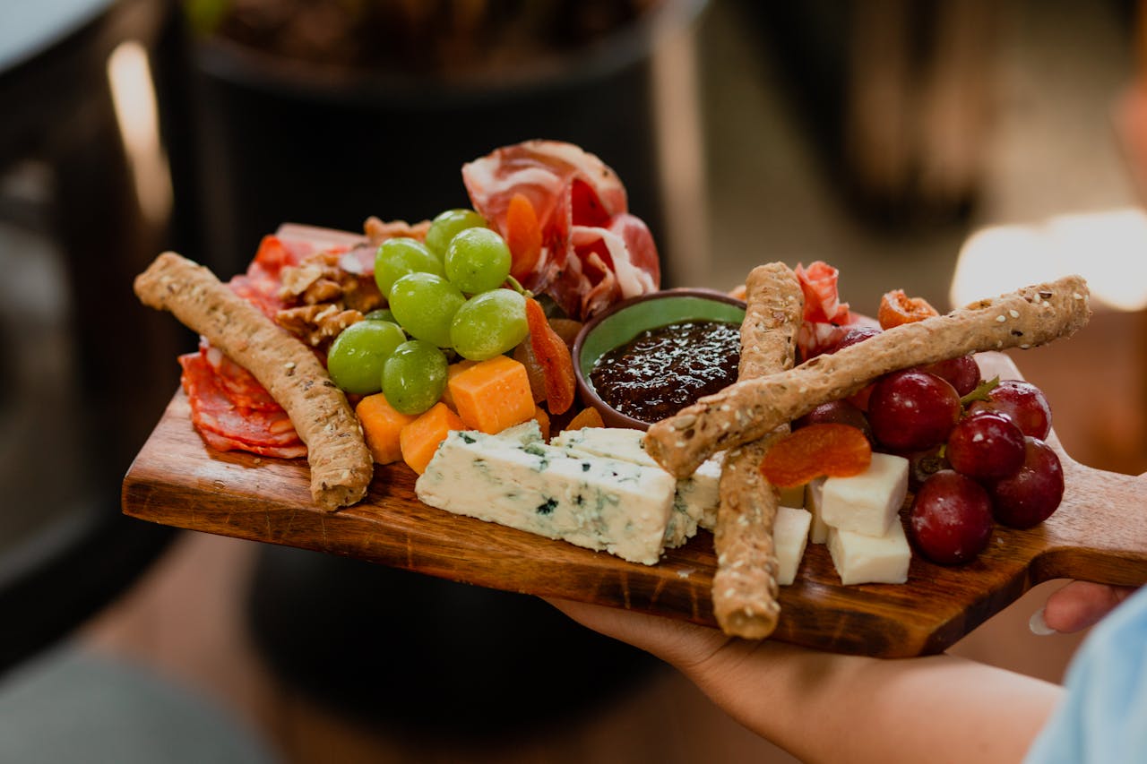 Charcuterie board with assorted cheeses, grapes, breadsticks, cured meats, dried fruits, and jam