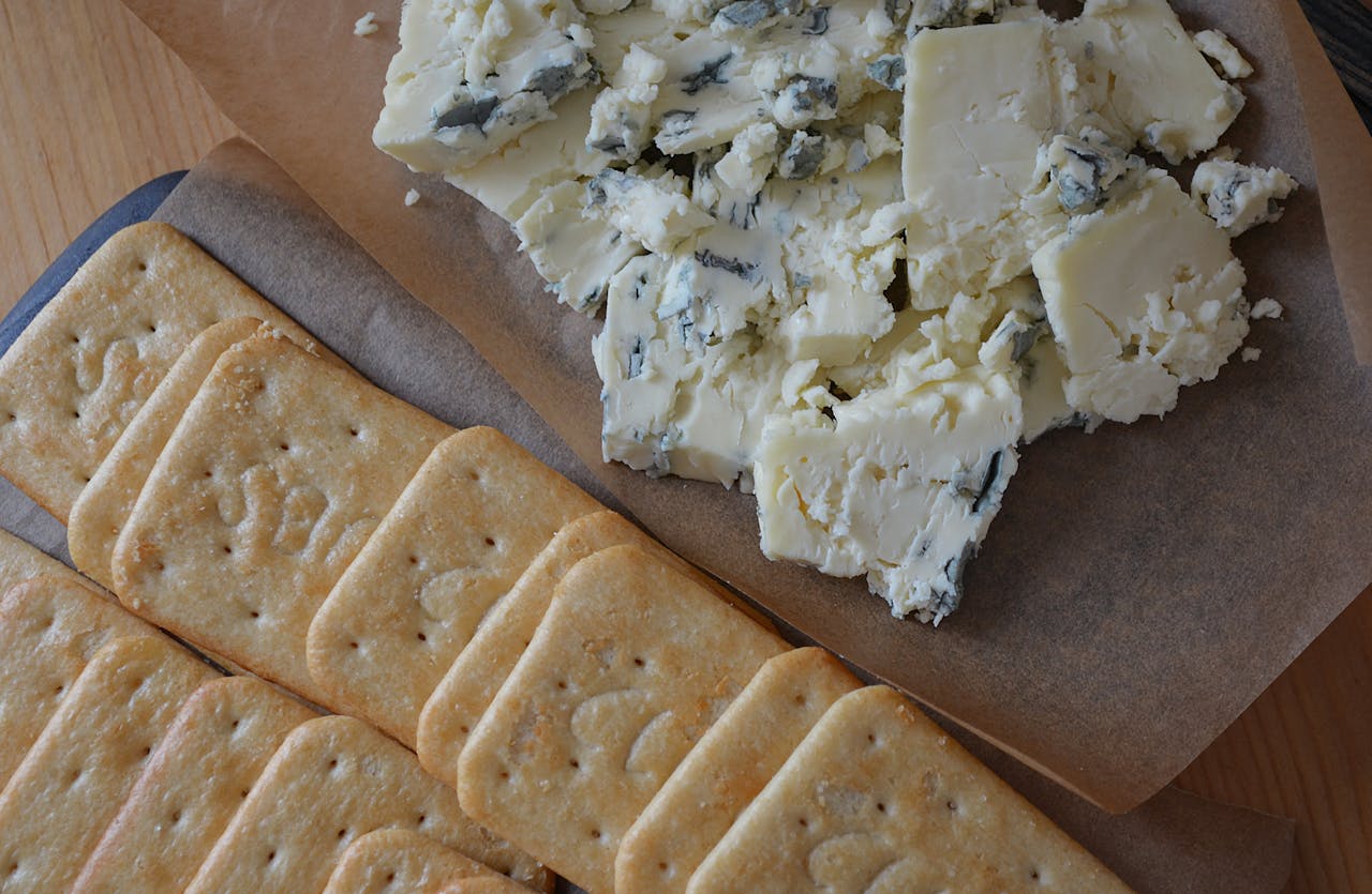 Crumbled blue cheese and rectangular crackers arranged on brown parchment paper