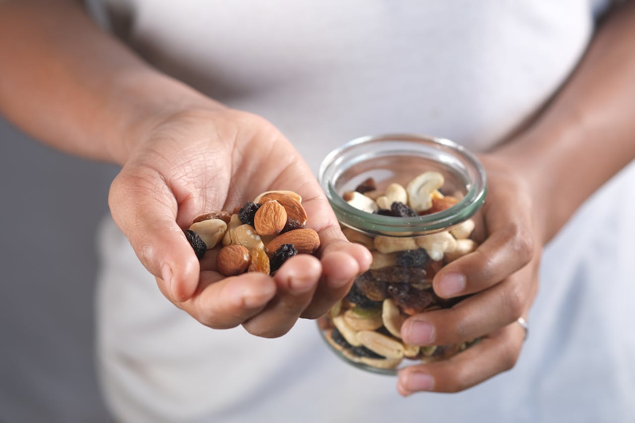 Hand holding a mix of nuts and dried fruits, with a jar of the same in the other hand