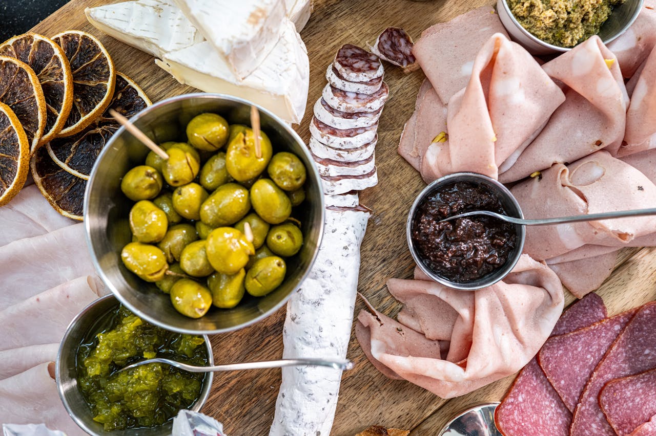Charcuterie board with green olives, cured meats, sliced cheese, spreads, and dried citrus slices