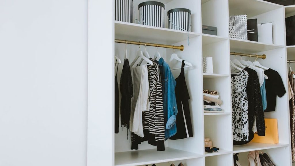  Organized white closet, hanging clothes on white hangers, striped storage boxes on the top shelf, shoes neatly arranged on side shelves, minimalist and tidy setup