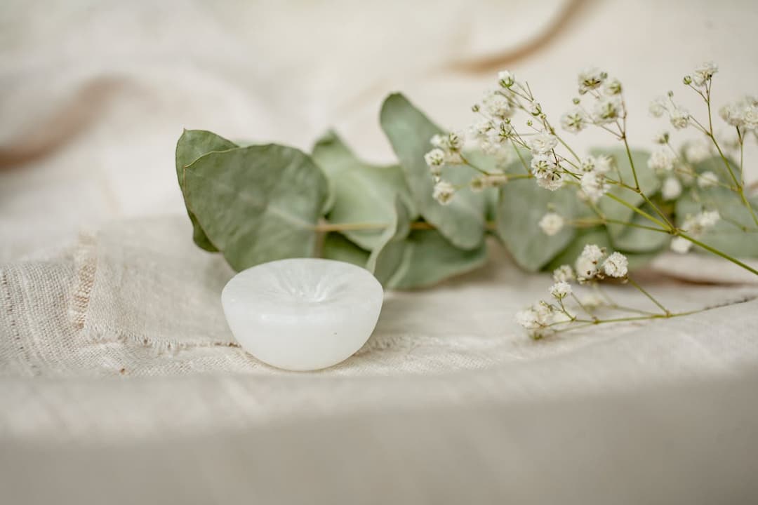 small white candle on beige fabric, with dried eucalyptus leaves and baby's breath flowers in soft natural light